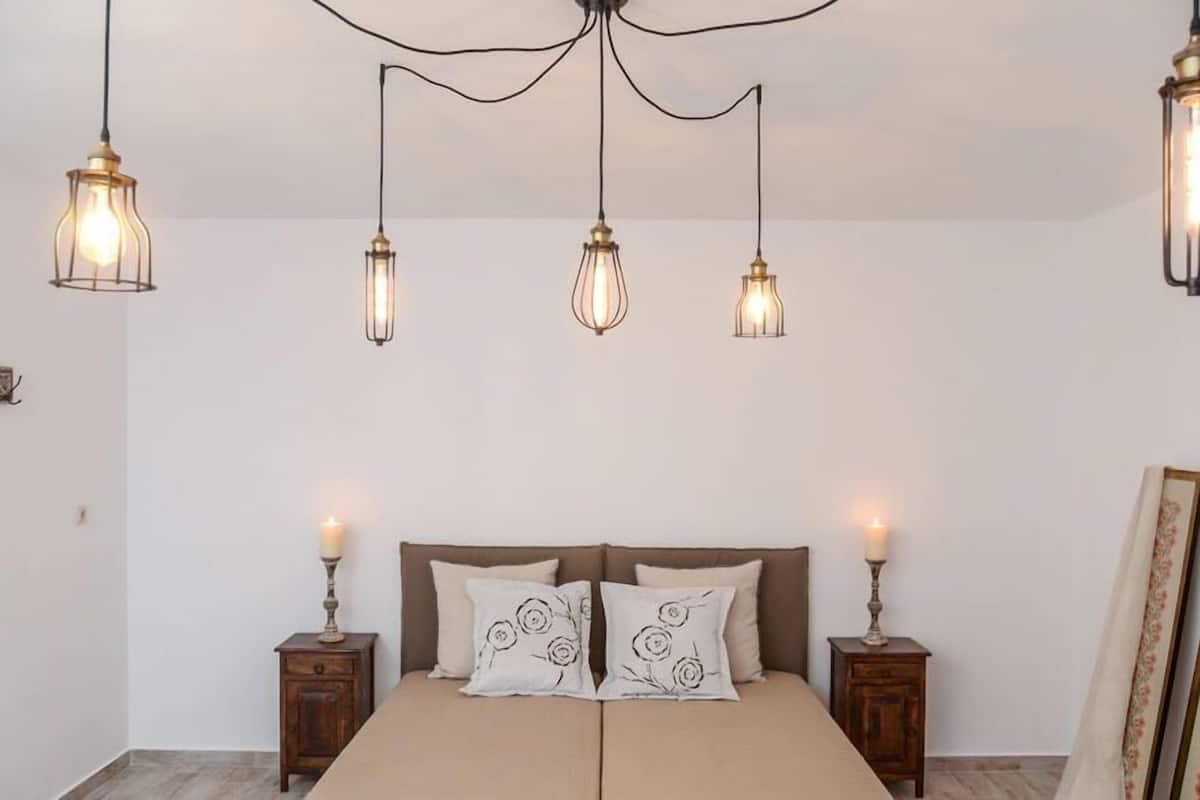 A bedroom with a bed, two bedside tables, and three hanging light fixtures.