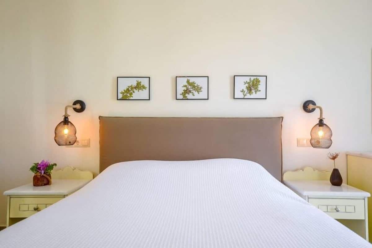 A neatly made bed with a white duvet, flanked by two bedside tables with lamps, and three framed botanical prints on the wall.