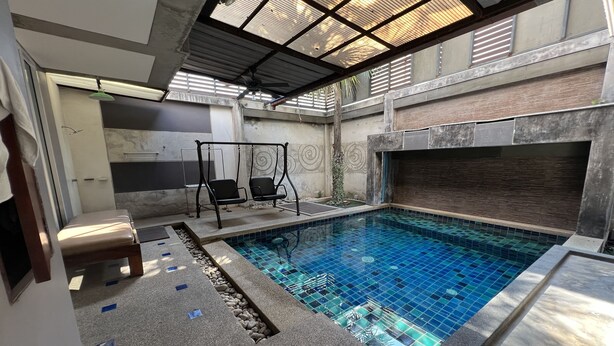 Una piscina con suelo de baldosas, una silla colgante y un banco.