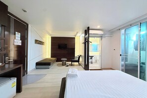 A hotel room with a bed, a seating area, a television, and a bathroom visible through a glass door. - Eurna Resort (Bangkok)