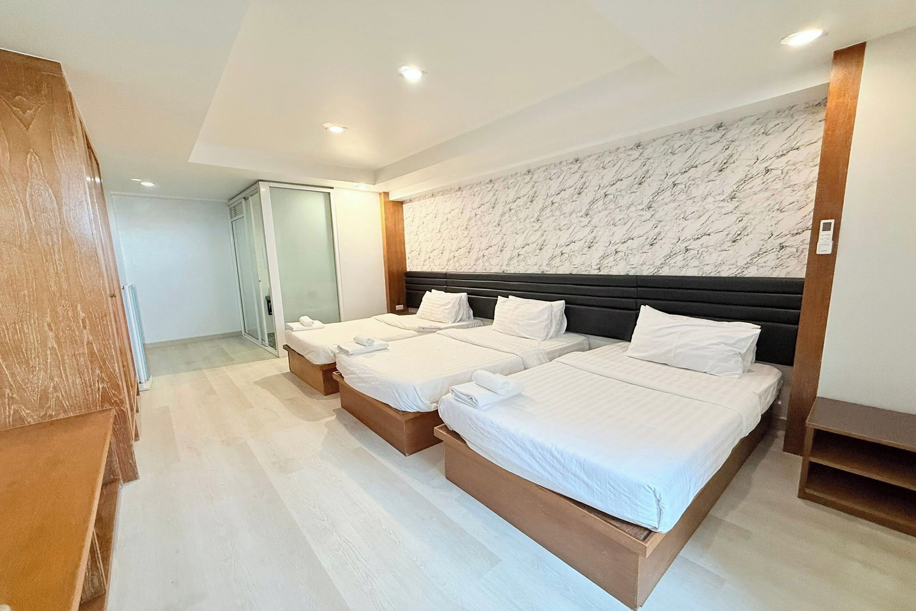 A hotel room with two beds, a marble-patterned wall, and a wooden wardrobe.