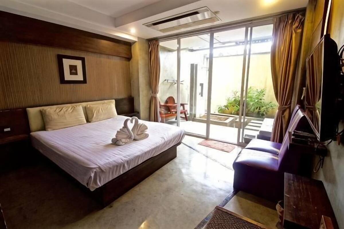 A hotel room with a large bed, a sofa, a TV, and a sliding glass door leading to an outdoor area.