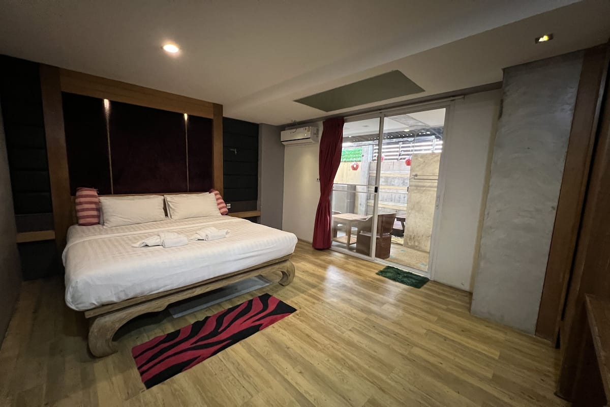 A bedroom with a bed, wooden floor, and a sliding glass door leading to an outdoor area.