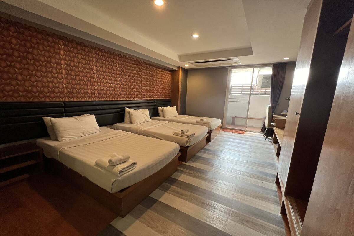A hotel room with three beds, a wooden headboard, a large window, and a wooden floor.