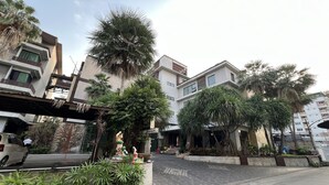 Un moderno edificio residencial con un camino cubierto, rodeado de exuberante vegetación y palmeras.