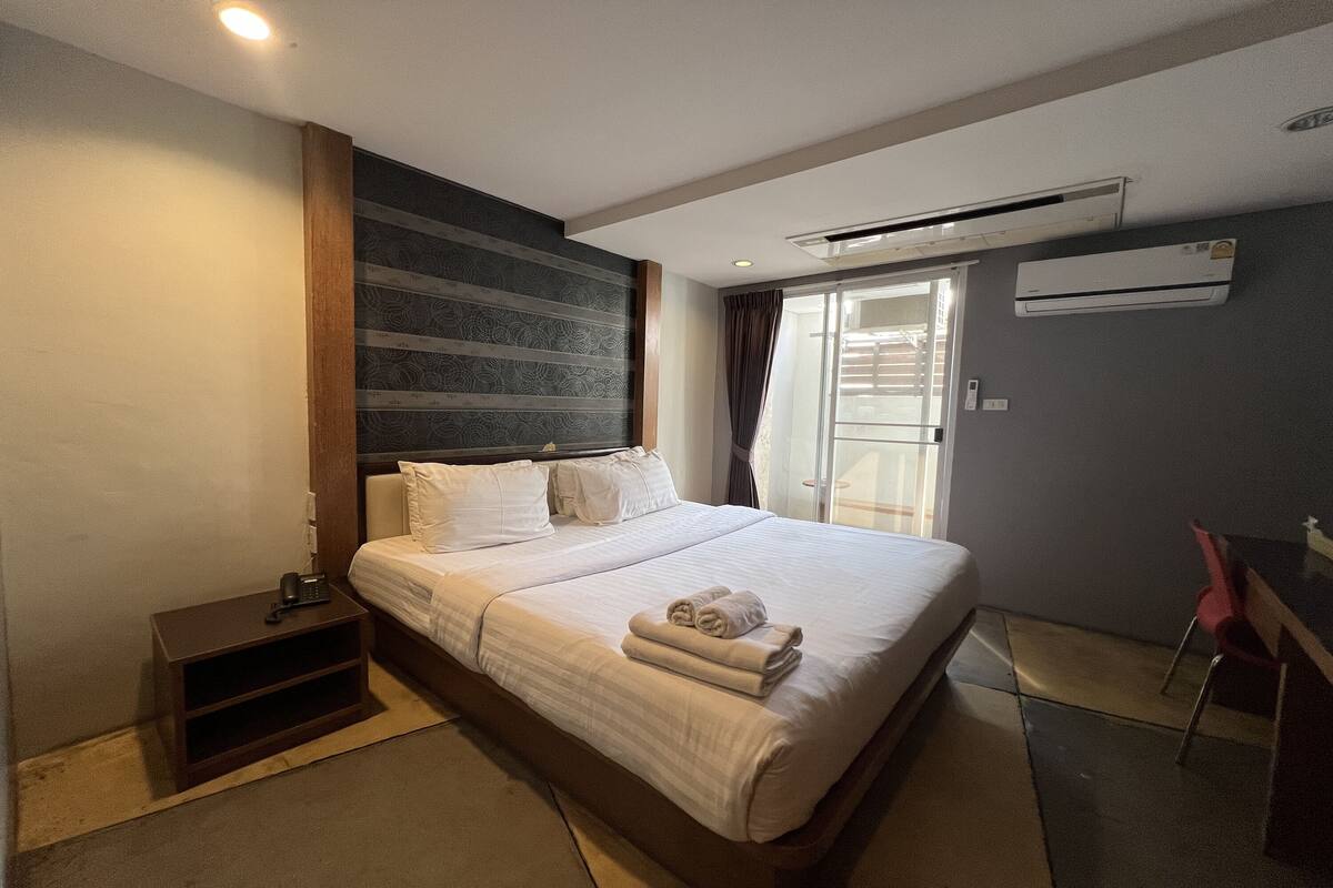A hotel room with a large bed, a bedside table, a chair, and a window with curtains.