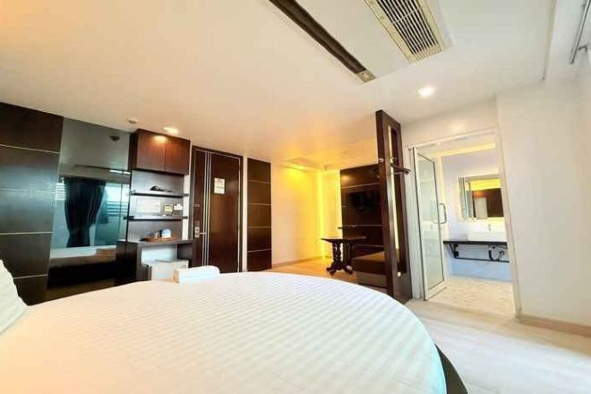 A hotel room with a large bed, a wardrobe, a desk, and a bathroom visible through an open door.