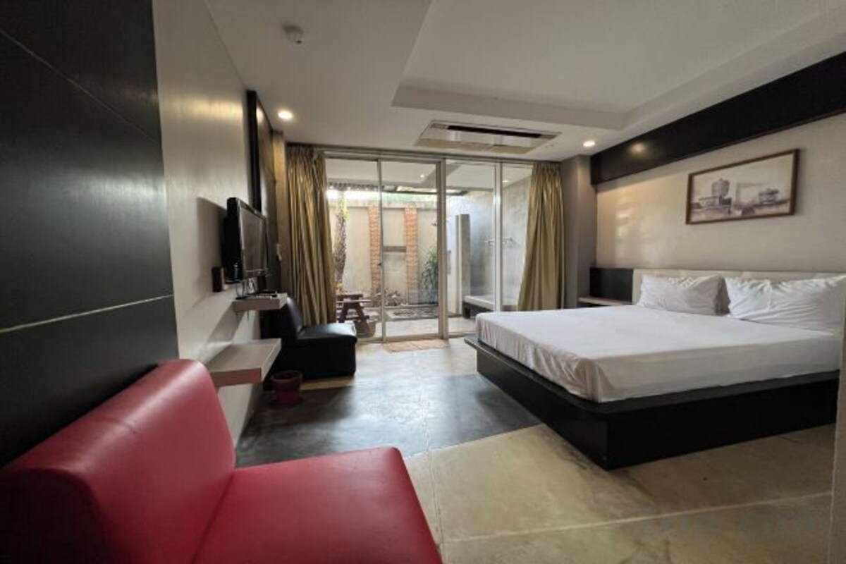A hotel room with a bed, a red sofa, a TV, and a sliding glass door leading to an outdoor area.