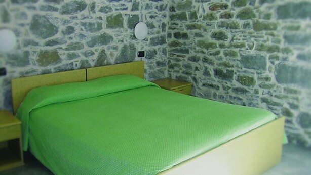 A room with a bed, wooden headboard, and a stone wall. - Albergo Val Dolo (Villa Minozzo)
