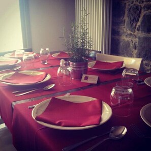 A dining table set with red napkins, plates, and cutlery, with a potted plant and a menu card. - Albergo Val Dolo (Villa Minozzo)