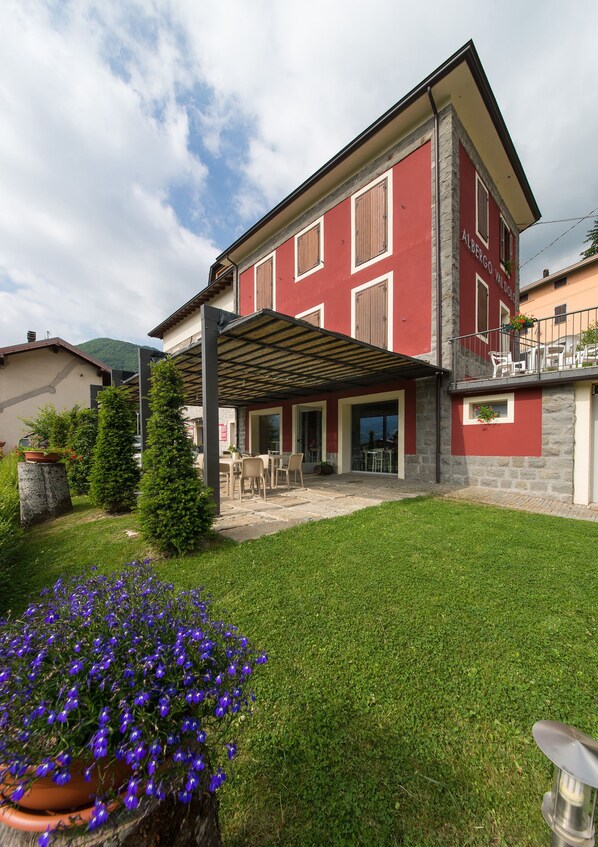 A two-story house with a covered patio, stone walls, and a well-maintained lawn. - Albergo Val Dolo (Villa Minozzo)