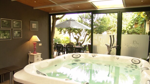Un jacuzzi en una habitación con techo de madera, una mesa con sillas afuera y cuadros en la pared.