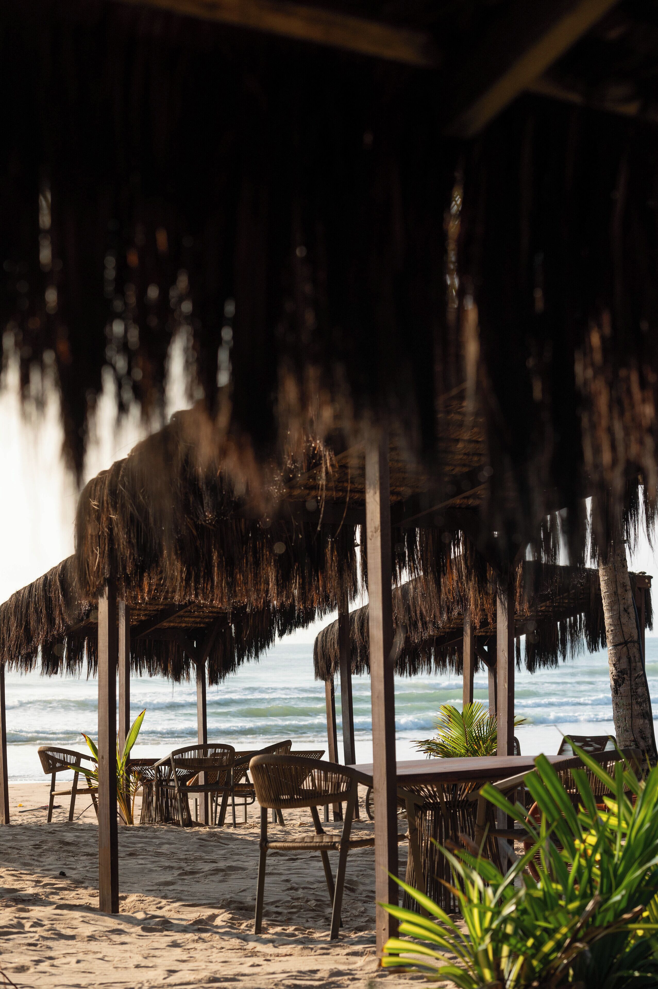 Un restaurante frente al mar con techos de paja y mobiliario de madera.