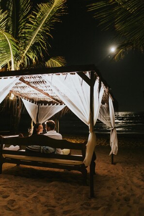 Una cabaña de playa con techo de paja y cortinas blancas, con vista al océano.