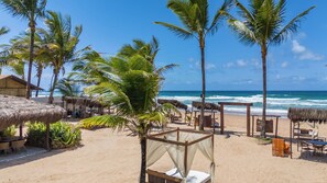 Una playa con cabañas de techo de paja, palmeras y vista al océano.