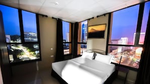Een hotelkamer met een groot bed, meerdere ramen en uitzicht op de stad.