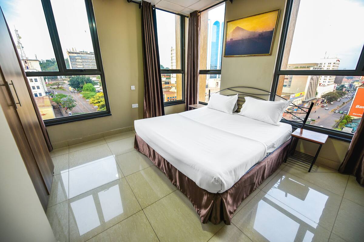 Habitación de hotel con una cama grande, un escritorio y una ventana con vista a la ciudad.
