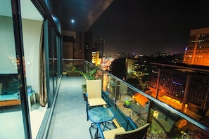 A balcony with a glass railing, wicker chairs, and a small table. - Boulevard Suites (Kampala)