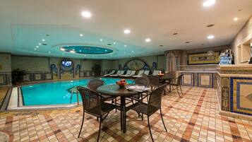 A pool area with a tiled floor, a round table with chairs, and a bar area with a tiled backsplash.
