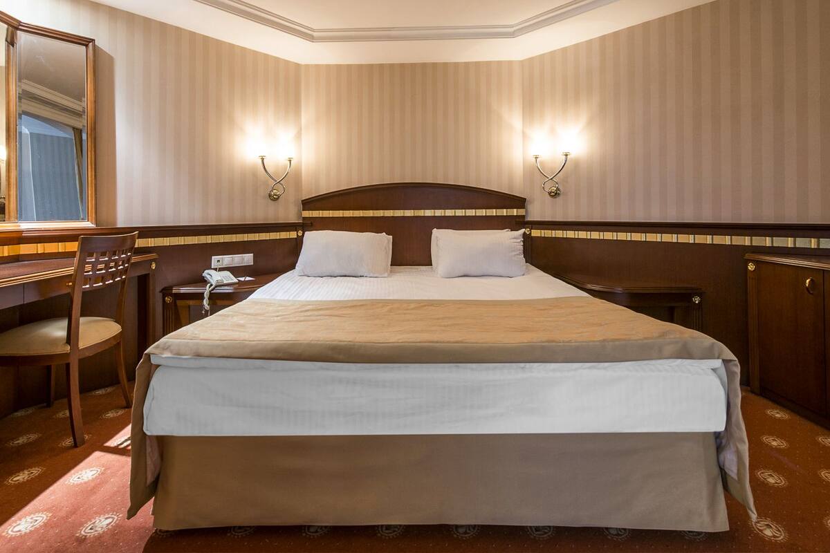 Habitación de hotel con una cama grande, un escritorio, una silla, un espejo y dos lámparas adosadas a la pared.