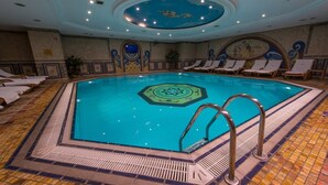 An indoor swimming pool with a geometric tile pattern, lounge chairs, and a decorative ceiling. - Akar International Hotel (Ankara)