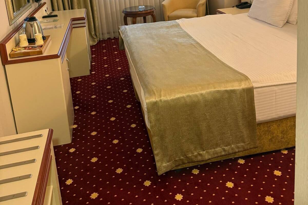 Habitación de hotel con cama, escritorio con teléfono, silla, televisor y ventana con cortinas.