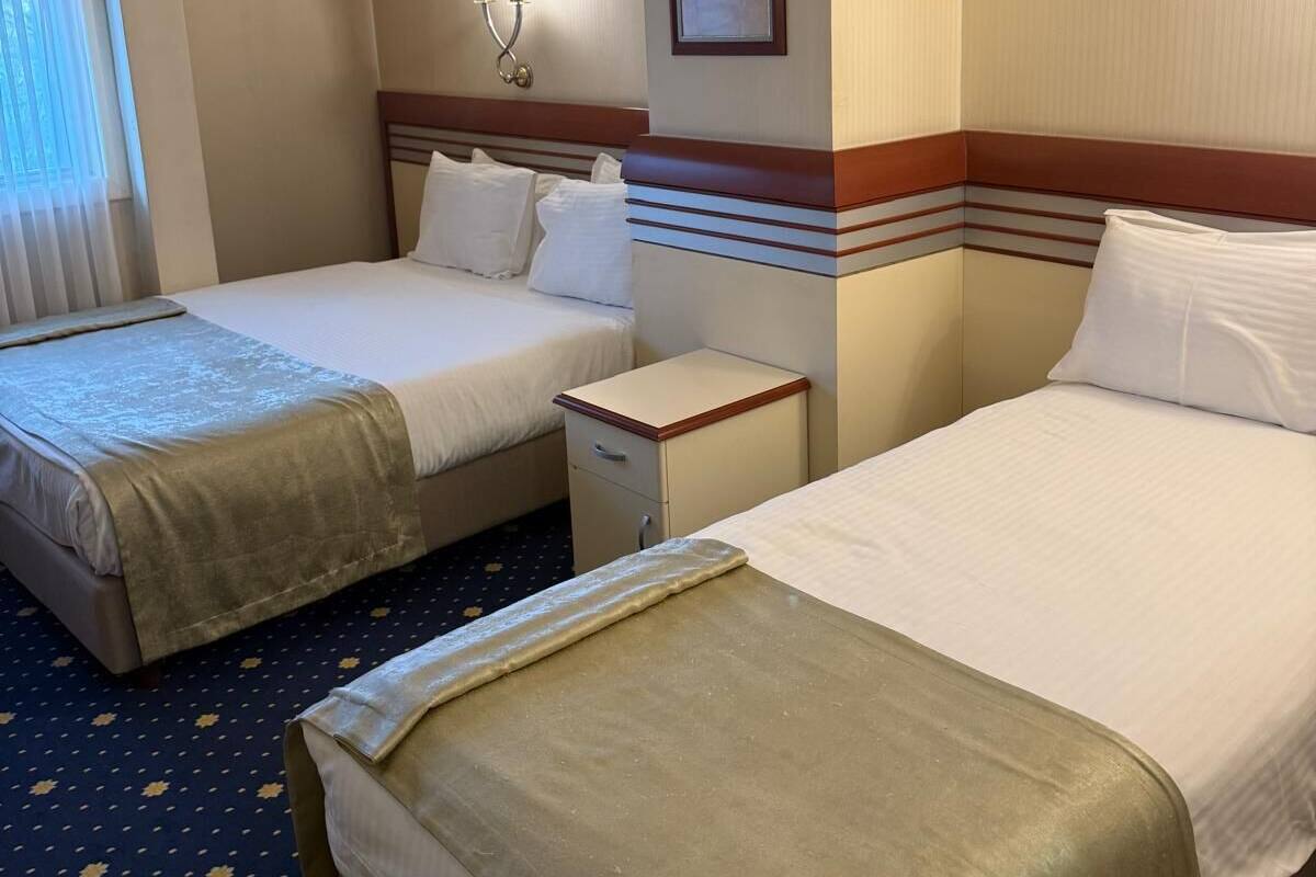 Habitación de hotel con dos camas, una mesita de noche, una lámpara de pared y un cuadro enmarcado.