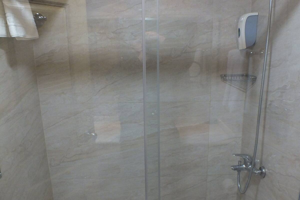 Cabina de ducha con cerramiento de vidrio, secador de manos y perchero para toallas.