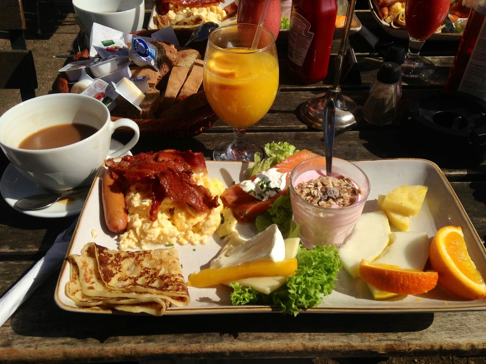 A breakfast tray with scrambled eggs, bacon, toast, a glass of orange juice, a salad, and a yogurt parfait.