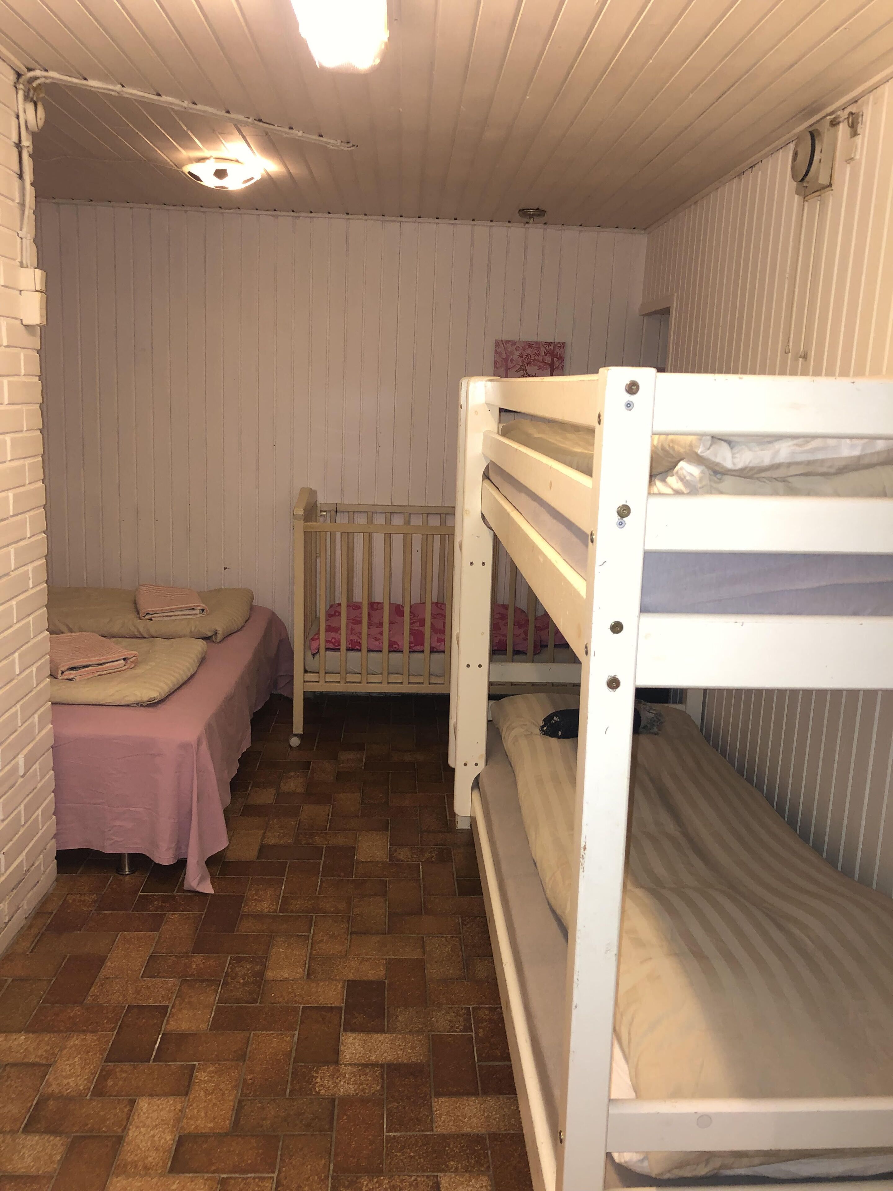 Een kleine, compacte kamer met twee stapelbedden, een enkel bed en een bakstenen muur.