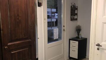 Un pasillo con una puerta de madera, una puerta blanca, un tapete negro, un mueble pequeño y una ventana que ofrece vistas al exterior.