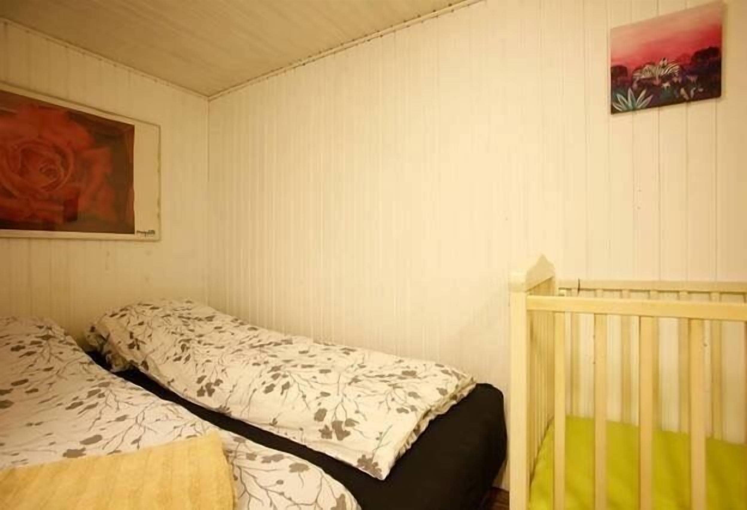 Una habitación con dos camas, una con una colcha estampada y la otra lisa. Hay una cuna con un colchón verde.
