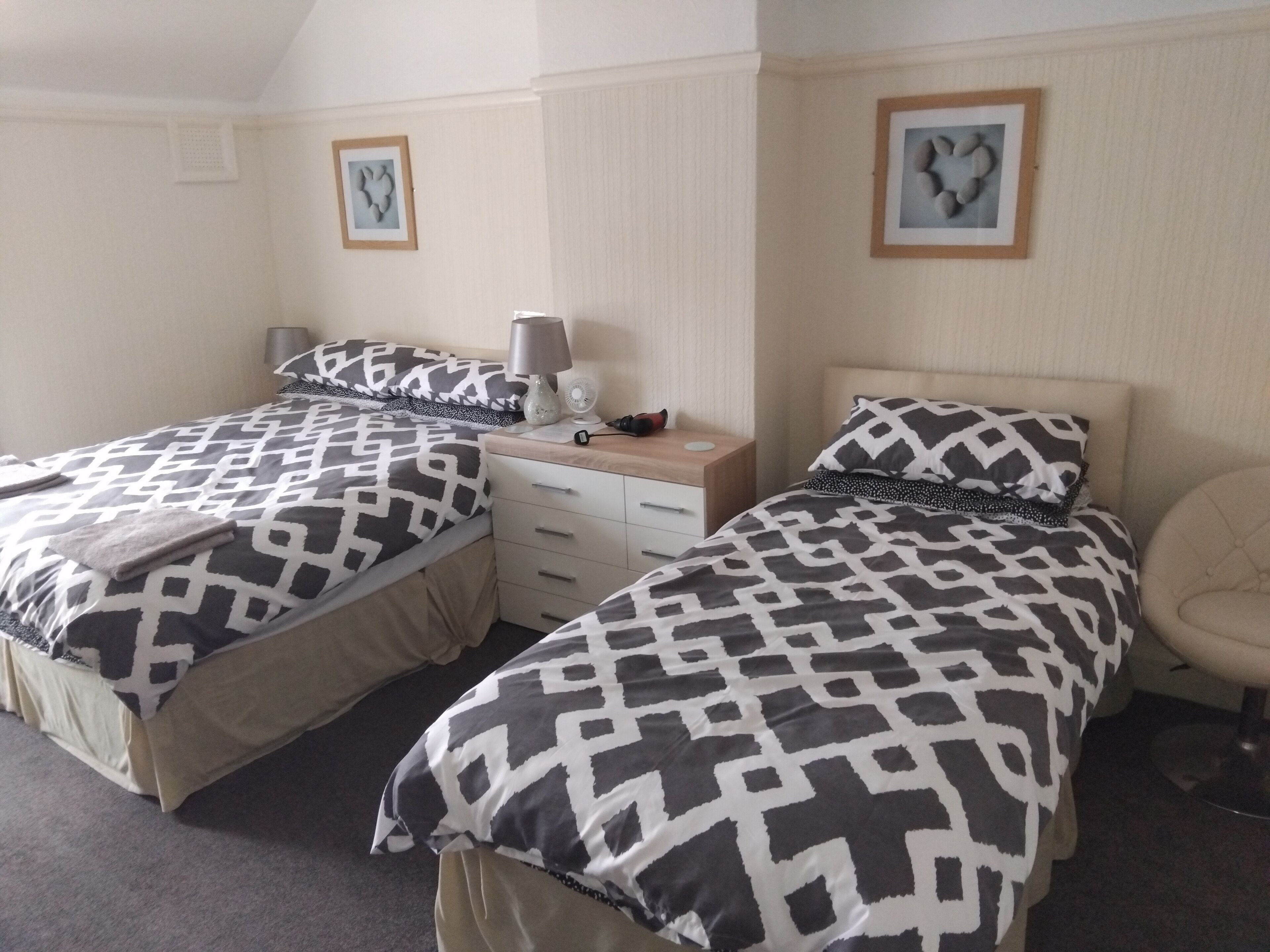 Quarto duplo com duas camas, cada uma com roupa de cama estampada, mesa de cabeceira com abajur e uma cadeira.