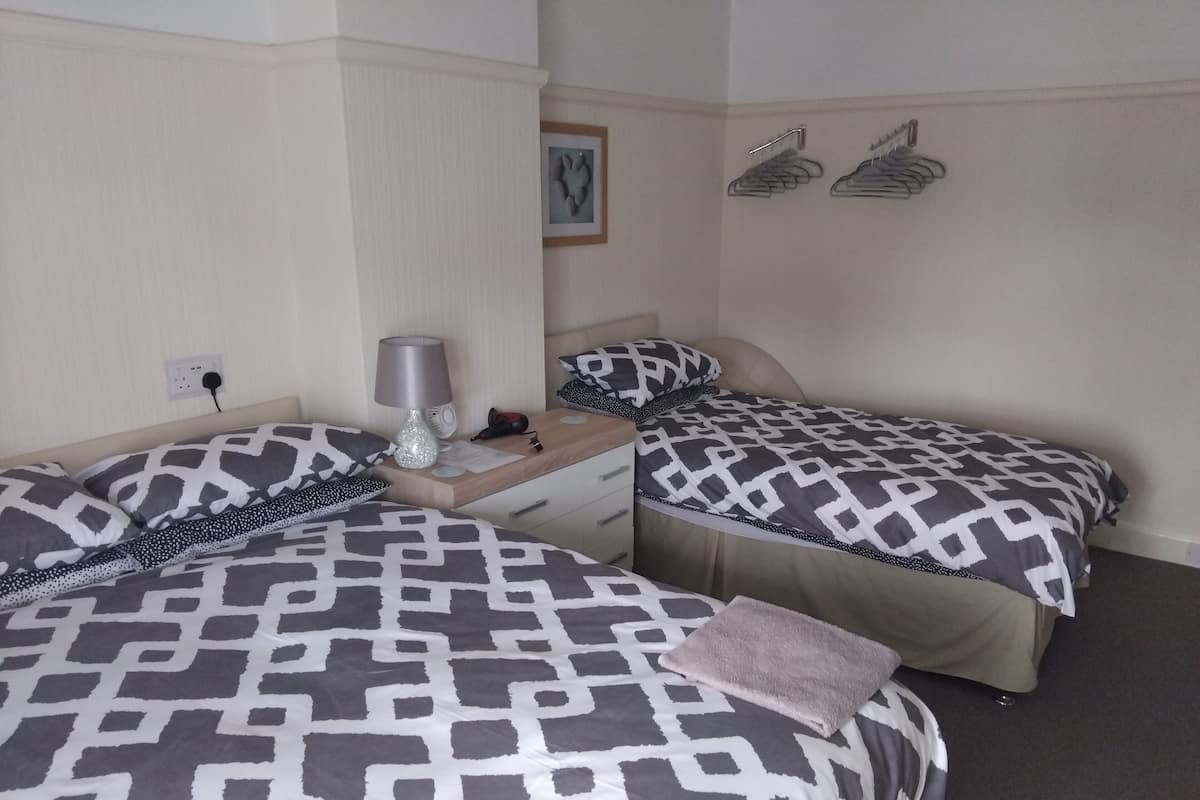 A hotel room with two beds, each with patterned bedding, a bedside table with a lamp, and a wall-mounted coat rack.