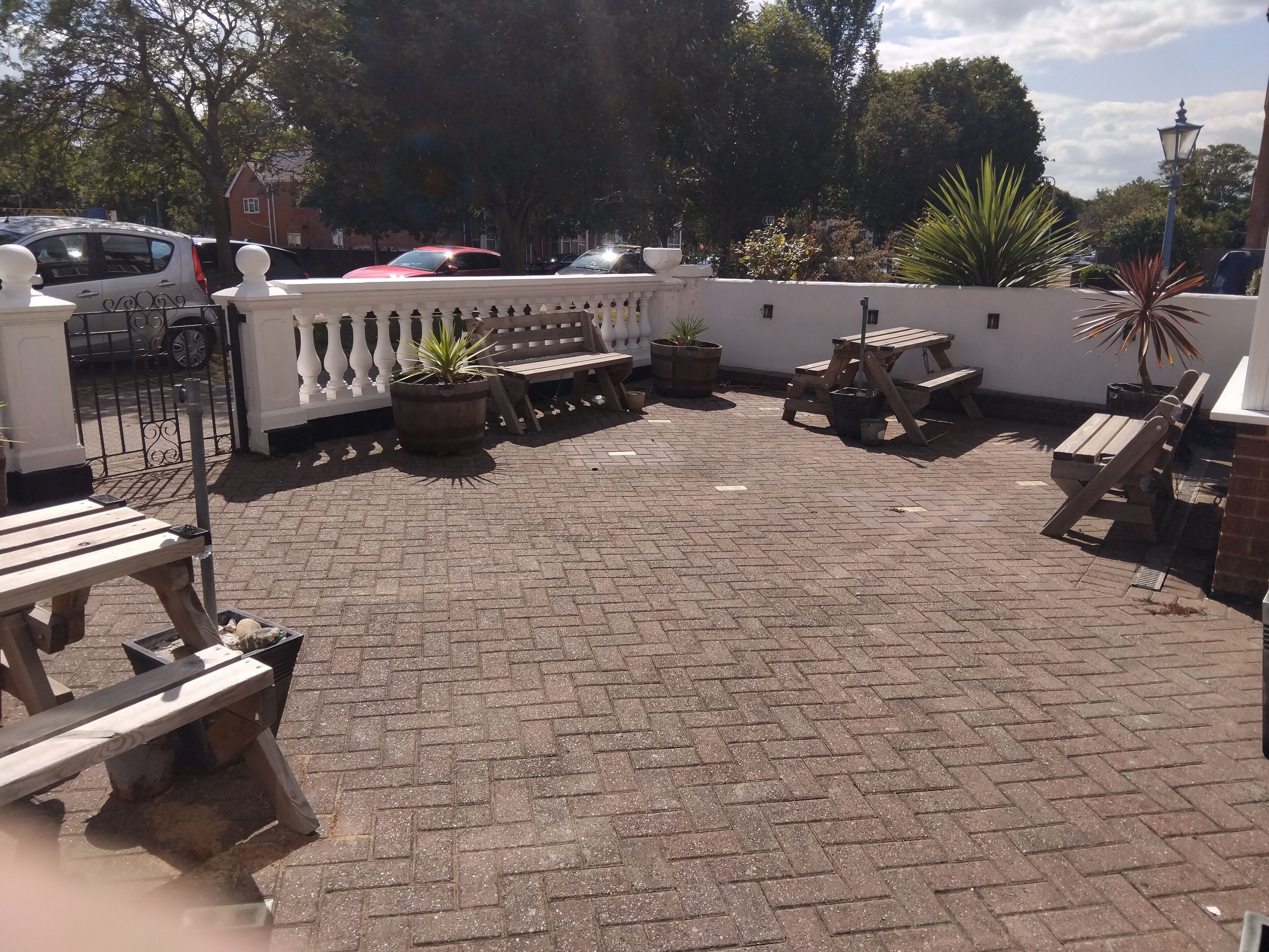 A patio area with brick flooring, wooden benches, and potted plants.