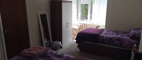 A bedroom with two beds, a wardrobe, a mirror, a television, and a window with a view of the outdoors.