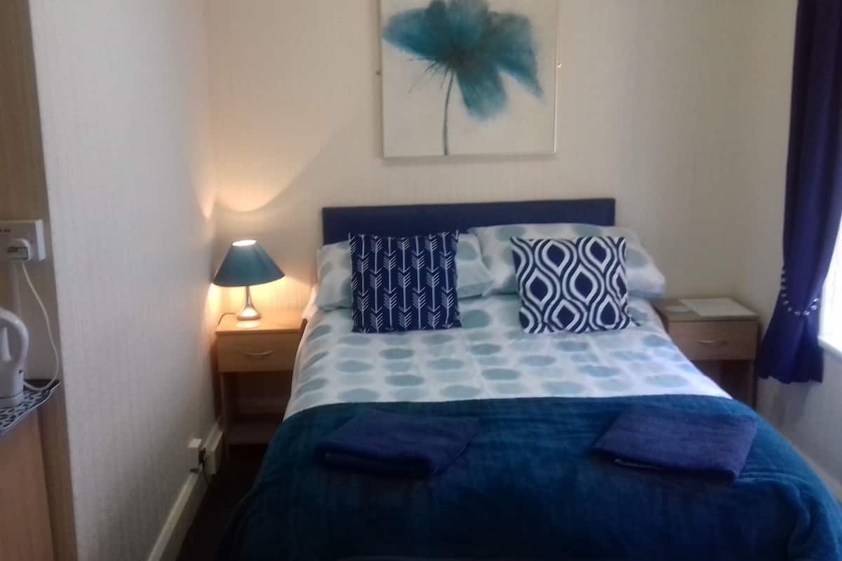A neatly made bed with patterned pillows, a bedside lamp, and a coffee maker on a table.