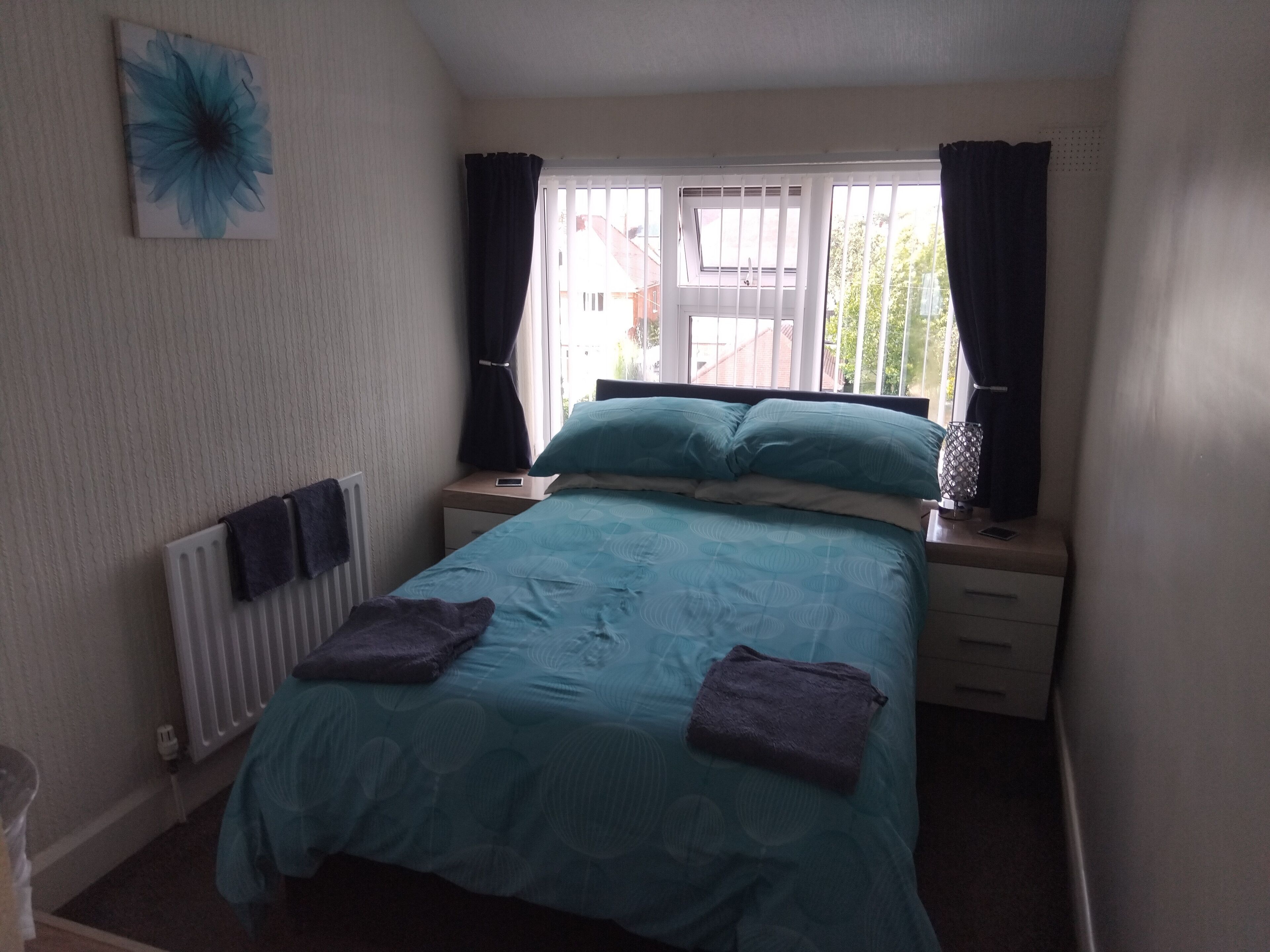 A bedroom with a bed, two bedside tables, a window with curtains, and a radiator.