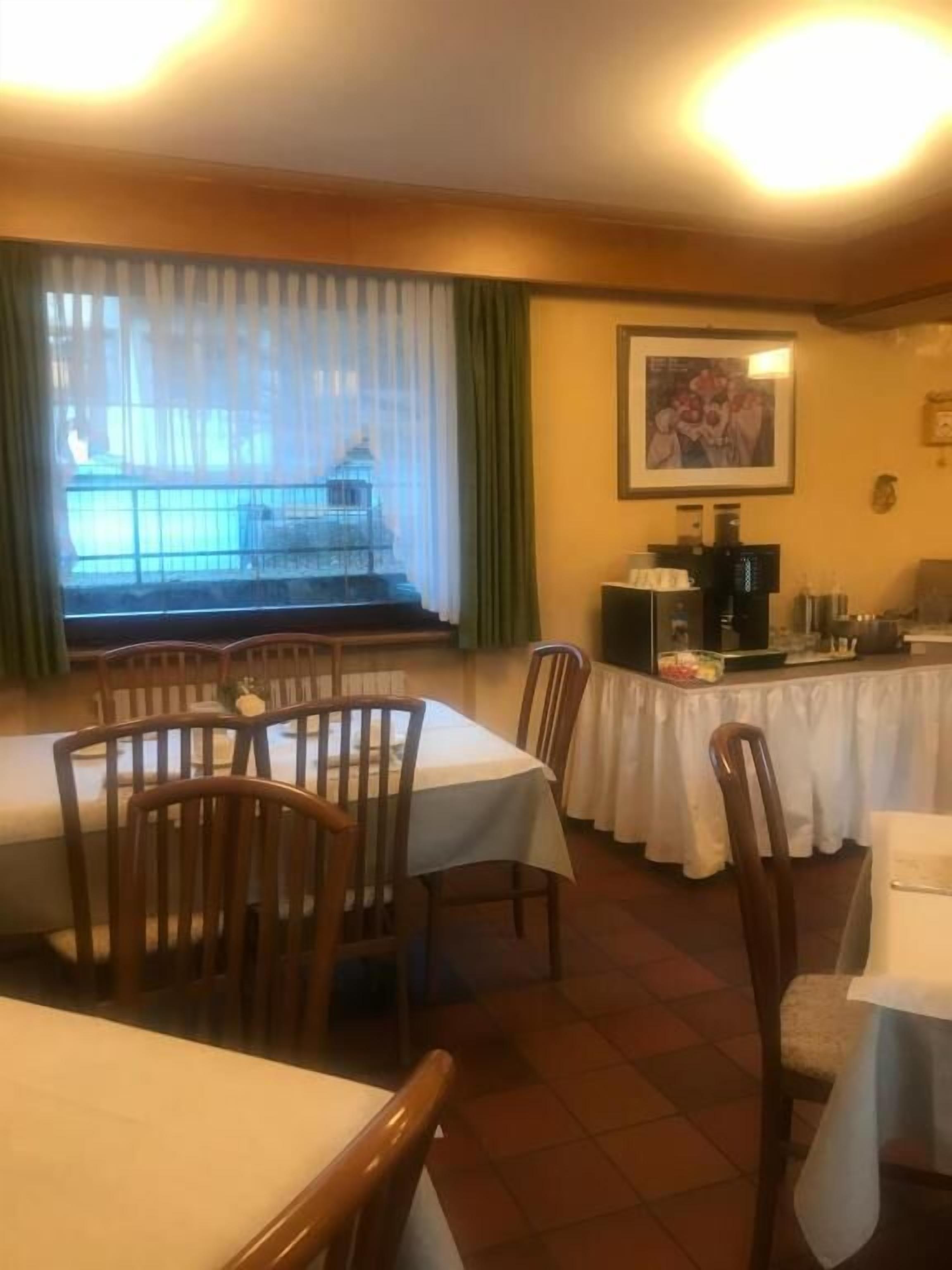 Un comedor con mesas y sillas, una cafetera y una ventana con cortinas.