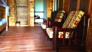 A log cabin interior with a wooden floor, a bed, and a seating area with patterned cushions.