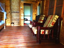 A log cabin interior with a wooden floor, a bed, and a seating area with patterned cushions.