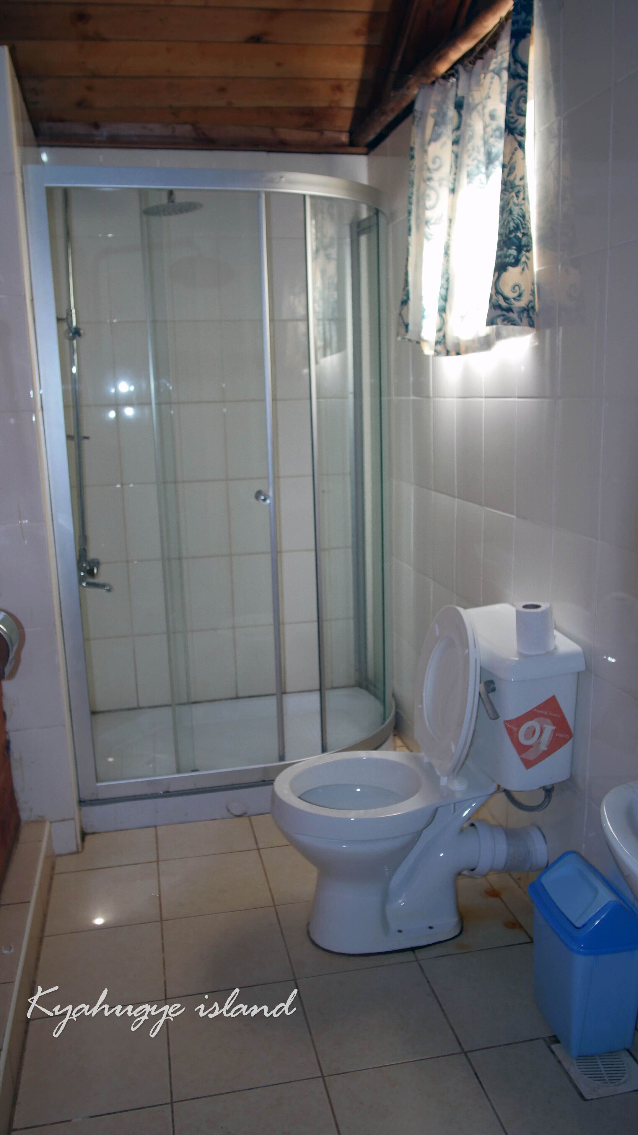 A bathroom with a glass-enclosed shower, a toilet, and a blue trash bin.