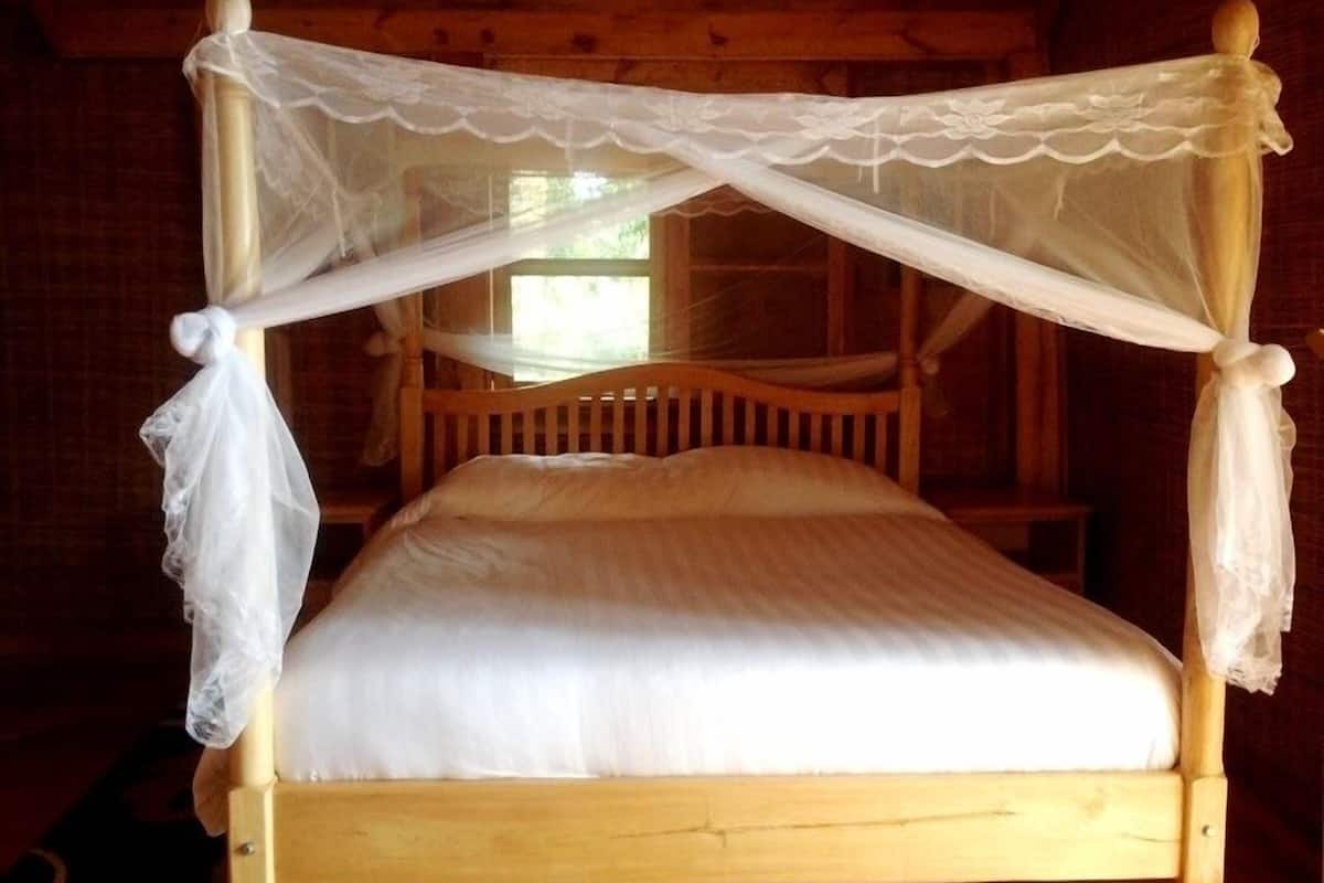 Uma cama de madeira com dossel e cortina branca, com detalhes em renda.