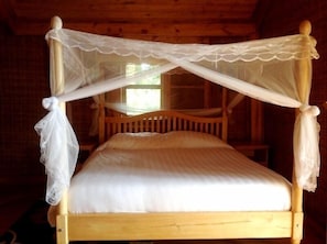 Una cama con dosel de madera, con dospilares y un dosel blanco con encaje.