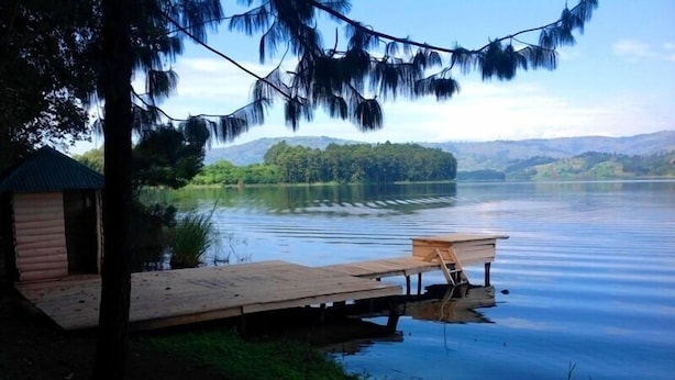 A lakeside cabin with a dock extending into the water, surrounded by greenery and hills in the background.