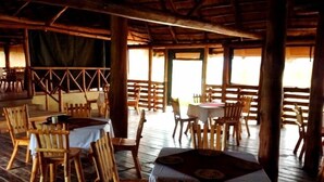 A restaurant with wooden furniture and a thatched roof. Tables and chairs are arranged for dining.