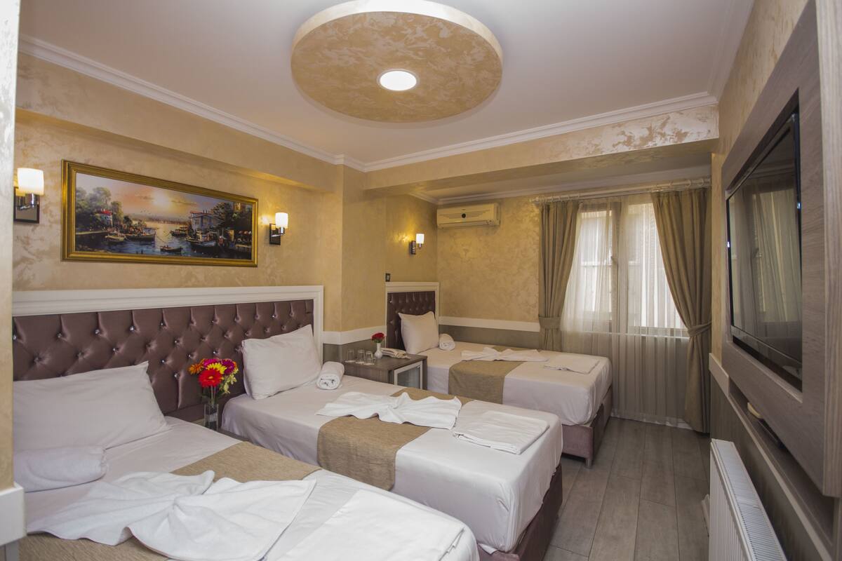A hotel room with three beds, a painting on the wall, a television, and a window with curtains.