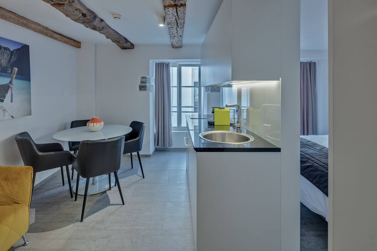 Moderni hotellihuone, jossa on ruokailutila, keittiö ja suuri ikkuna.