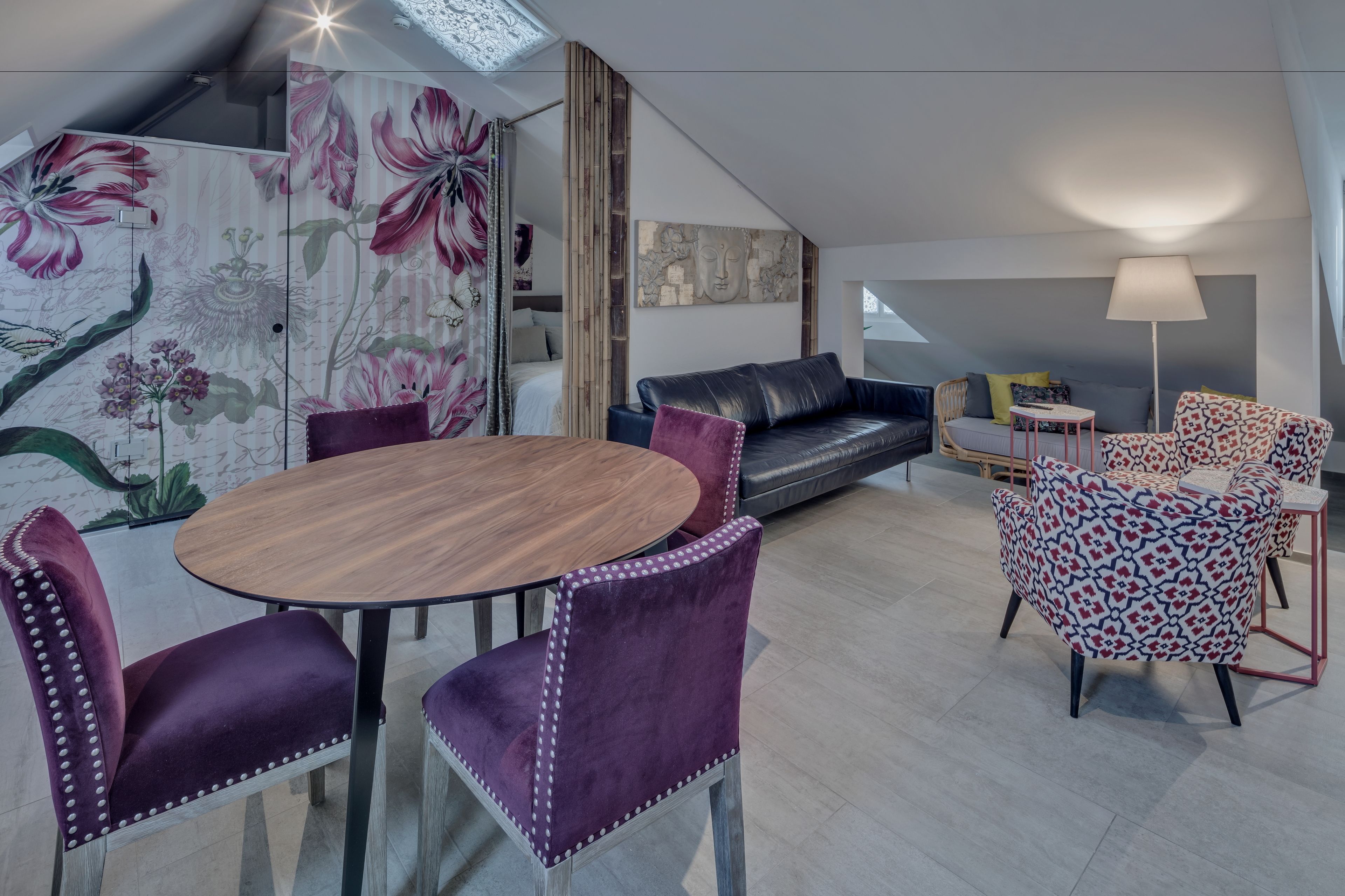 Ein modernes Interieur mit einem runden Holztisch, violetten Polsterstühlen, einer schwarzen Ledersofa und gemusterten Sessel.