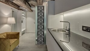 A modern kitchen with a stainless steel sink, a patterned column, and a yellow armchair. - The Residence La Cittadella (Baden)